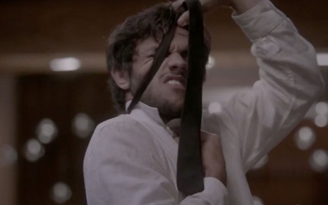 O ator Felipe Simas tira a gravata pela cabeça caracterizado como o Jonatas em cena de Totalmente Demais