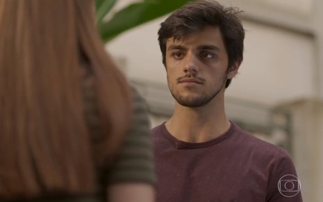O ator Felipe Simas, com expressão séria, usando uma camiseta roxa, em cena como Jonatas em Totalmente Demais