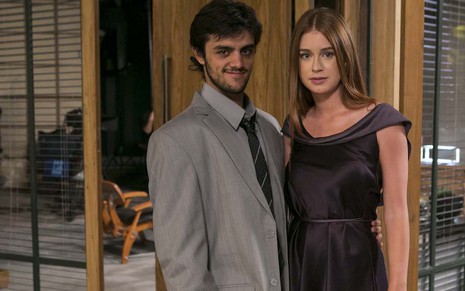 O ator Felipe Simas, com um terno cinza grande para seu tamanho, posa com Marina Ruy Barbosa em cenário de Totalmente Demais
