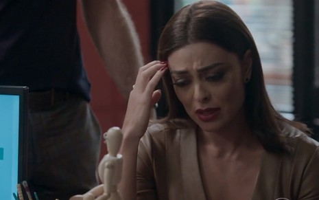 Juliana Paes com expressão triste apoiada à mesa em cena da novela Totalmente Demais em que interpreta Carolina
