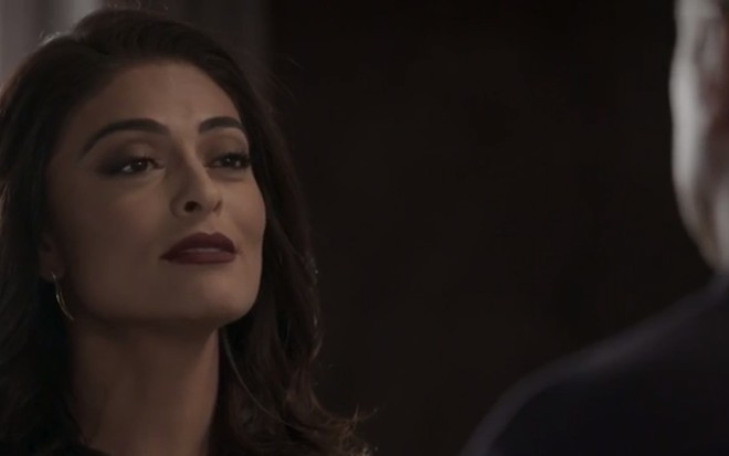 A atriz Juliana Paes, com blusa preta e batom vermelho, com expressão de triunfo, em cena como Carolina em Totalmente Demais