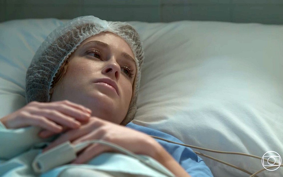 Eliza (Marina Ruy Barbosa) deitada em uma cama de hospital com touca no cabelo em cena de Totalmente Demais