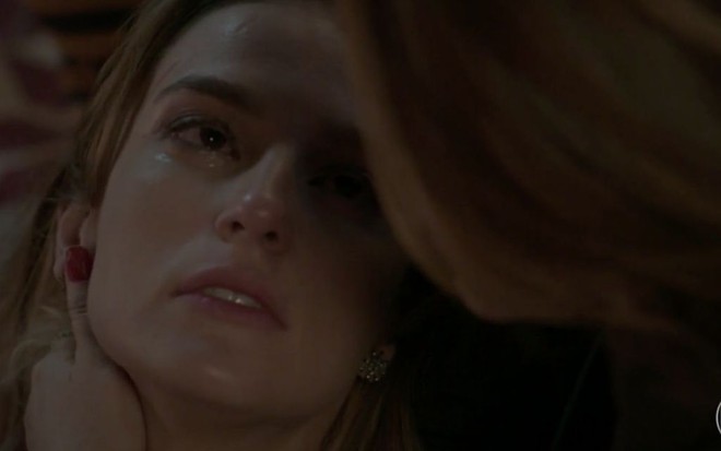 A atriz Priscila Steinman desfalecida como a personagem Sofia na novela Totalmente Demais, da Globo; a atriz Vivianne Pasmanter, como a Lili, aparece de costas segurando Priscila
