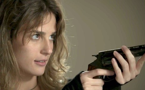 Com cara de maluca, Sofia (Priscila Steinman) aponta uma arma de fogo em cena de Totalmente Demais