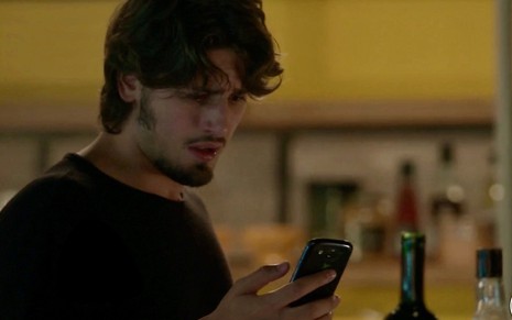O ator Daniel Rocha, de cabeça baixa, olhar para celular como o personagem Rafael da novela Totalmente Demais, da Globo
