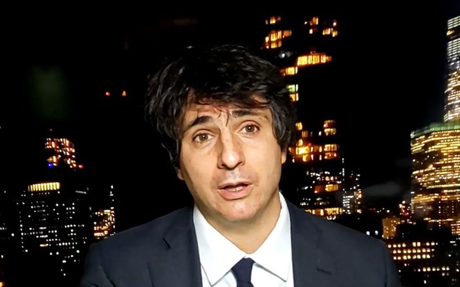 O jornalista Guga Chacra de terno e gravata escura, durante exibição de jornal Em Pauta