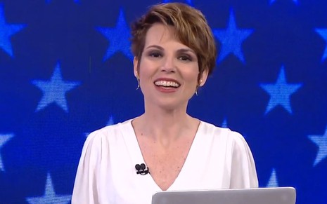 Gloria Vanique sorridente, de blusa branca, em um cenário azul com estampas de estrelas
