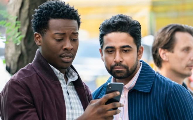 Ao lado de Suraj Sharma, Brandon Michael Hall segura com a mão direita um celular; os dois olham o aparelho com pesar