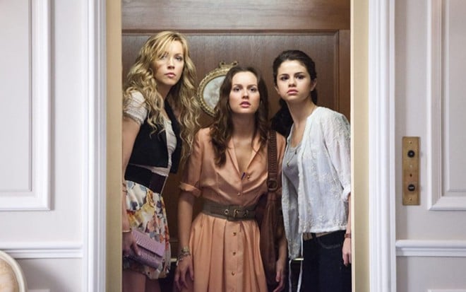 Katie Cassidy, Leighton Meester e Selena Gomez lado a lado, em pé, olhando para frente parecendo surpresas