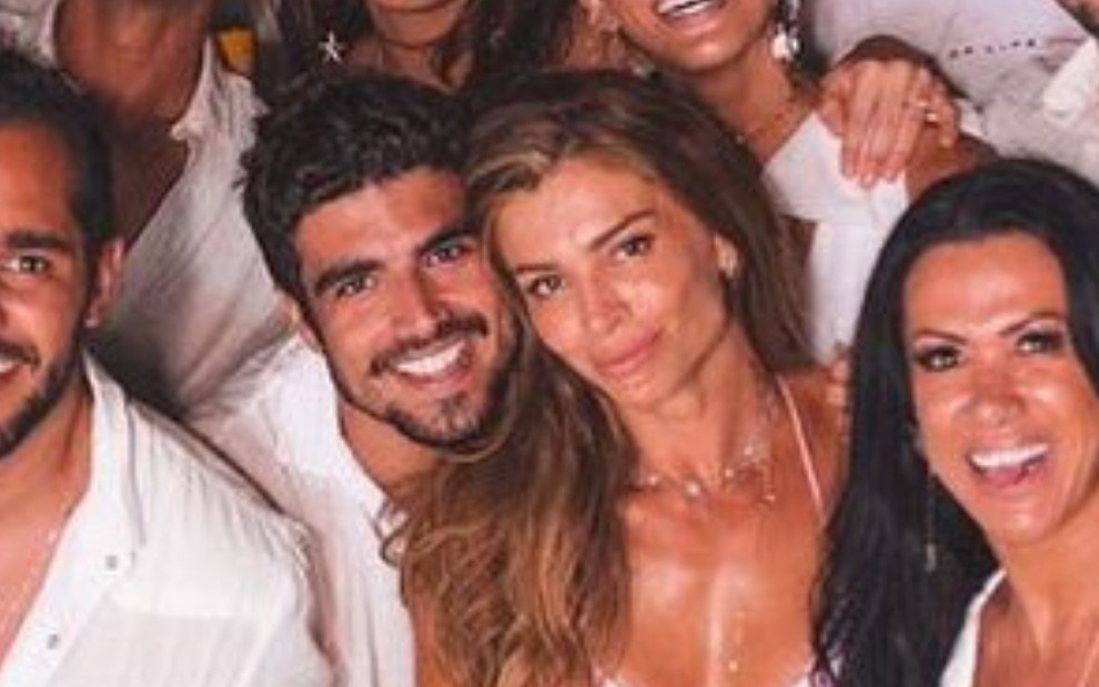Caio Castro e Grazi Massafera vestidos de branco com um grupo de amigos durante o Réveillon