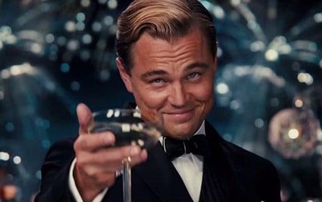 Leonardo DiCaprio estende mão com um copo em cena do filme O Grande Gatsby (2013)