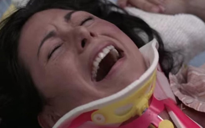 Deitada em um chão com um colar protetor no pescoço, a atriz Arlene Tur finge ter um orgasmo na série Grey's Anatomy