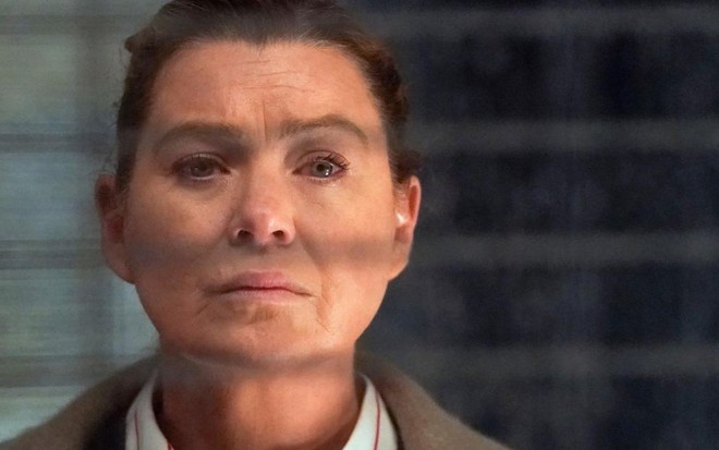 Dentro de uma sala de hospital, observada através de uma janela com persiana aberta, Ellen Pompeo aparece em Grey's Anatomy