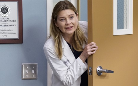 Com sutileza, Ellen Pompeo abre porta de uma sala dentro do hospital Grey Sloan na série Grey's Anatomy