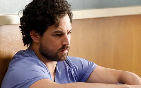 Desolado e sentado no chão, um descabelado Giacomo Gianniotti fica enfurecido em cena de Grey's Anatomy