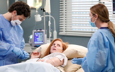 Com máscara no rosto, Giacomo Gianniotti em cena com Sarah Rafferty, que olha assustada para Ellen Pompeo em Grey's Anatomy