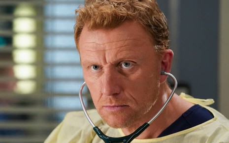 O ator Kevin McKidd com um estetoscópio nos ouvidos e vestindo avental médico em cena da 16ª temporada de Grey's Anatomy