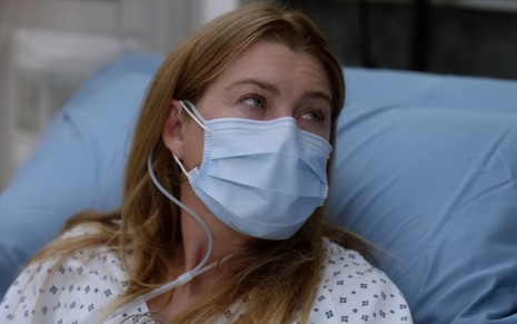 Ellen Pompeo, intérprete de Meredith Grey, de máscara deitada na cama do hospital olhando para o lado