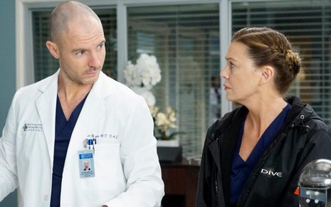 Com um avental de médico, Richard Flood conversa com Ellen Pompeo, com uma roupa mais despojada, em cena de Grey's Anatomy