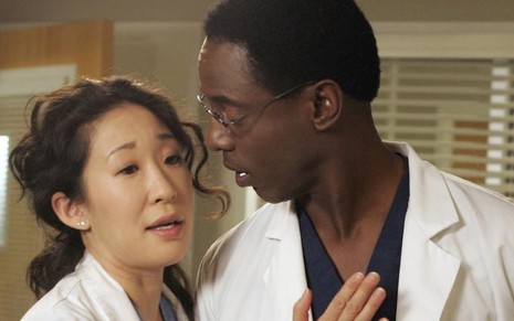 Dentro de um hospital e vestidos como médicos, Sandra Oh e Isaiah Washington se abraçam em cena de Grey's Anatomy