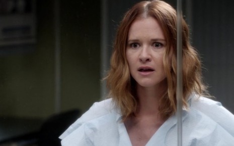 Sarah Drew assustada por trás de uma parede de vidro que a isolou em um episódio de Grey's Anatomy