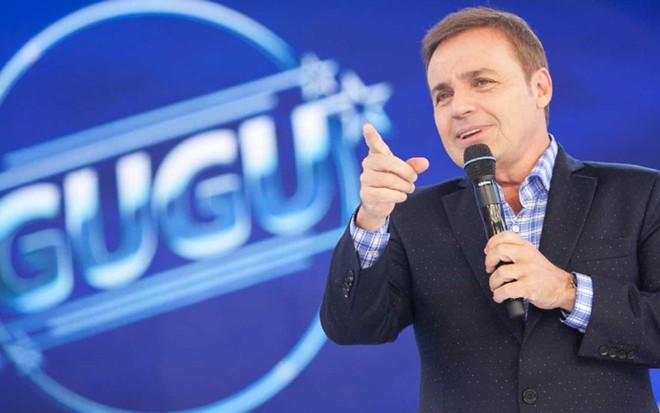 Gugu Liberato no cenário de um programa de televisão, vestindo um terno e com um dos dedos apontados para frente