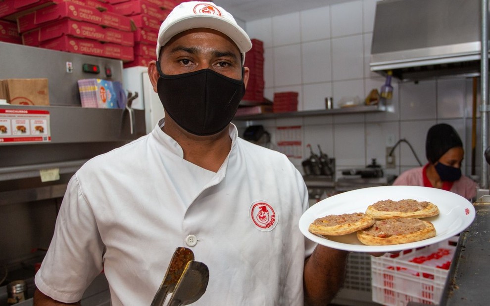 De máscara, o chefe de cozinha Antonio Paulo Mendes da Silva segura prato com três esfirras no Habib's