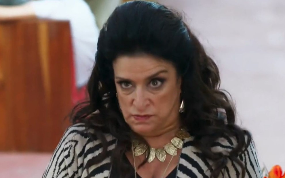 A atriz Grace Gianoukas usa um topete enorme nos cabelos e faz expressão furiosa em cena como Teodora em Haja Coração