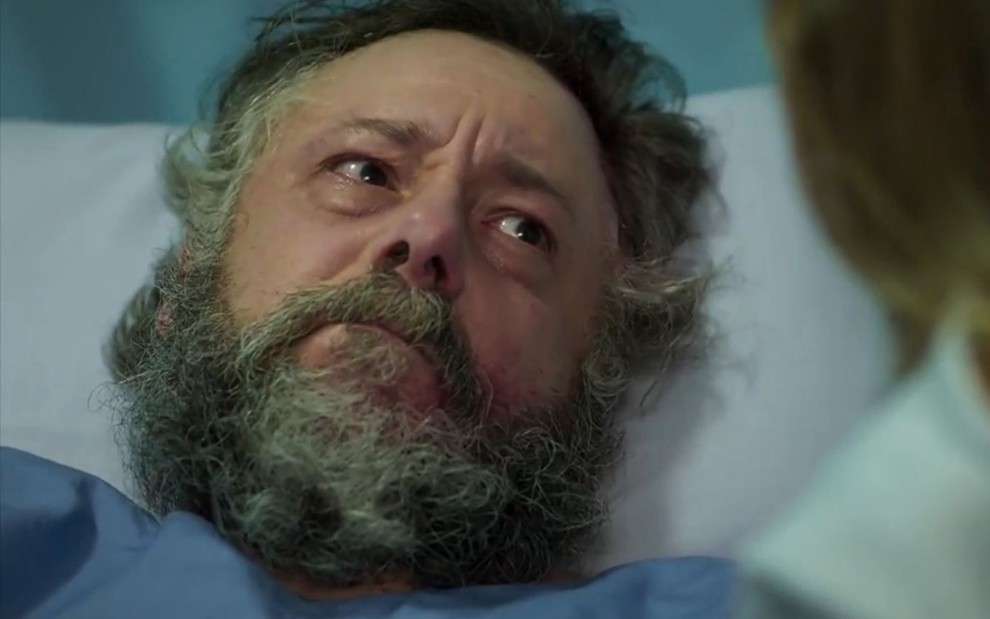 O ator Mario Hermeto aparece deitado em uma cama de hospital e faz expressão de tristeza em cena como Afonso de Haja Coração