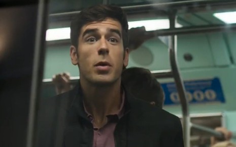 O ator Marcos Pitombo está dentro de um vagão do metrô com a porta fechada; ele tenta falar com a pessoa do outro lado da porta