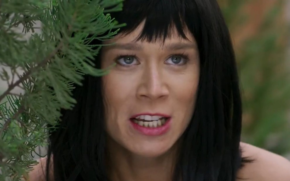A atriz Mariana Ximenes usa uma peruca preta chanel e se esconde atrás de uma planta em cena como Tancinha de Haja Coração