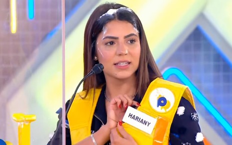 Hariany Almeida com o cabelo sujo de torta, vestindo um colete amarelo