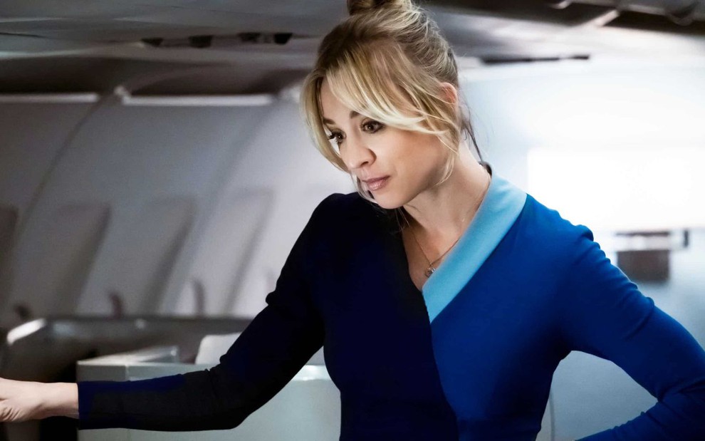 Kaley Cuoco está vestida de comissária de bordo dentro de um avião na série The Flight Attendant