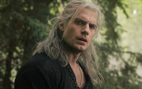 O ator Henry Cavill com expressão blasé e cabelos na altura dos ombros em cena de The Witcher
