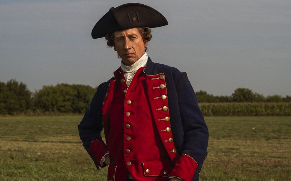 Vestido com roupas de batalha de época, Nicholas Rowe posa com expressão imponente caracterizado como George Washington