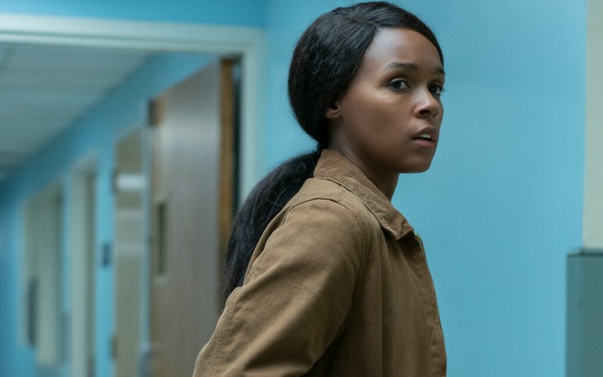 Com uma jaqueta marrom e cabelo preso em um rabo de cavalo, Janelle Monáe para no meio de um corredor vazio de um prédio em Homecoming