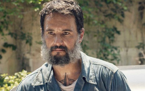 Rodrigo Santoro aparece em cena de Reprisal com uma barba grisalha e dessajeitada, vestindo uma jaqueta jeans