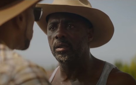 Idris Elba usa chapéu de cowboy enquanto conversa em cena do filme Alma de Cowboy, da Netflix