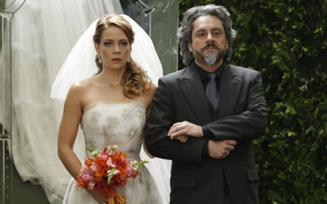 A atriz Leandra Leal, vestida de noiva, segura um buquê e dá o braço para Alexandre Nero em cena de casamento em Império