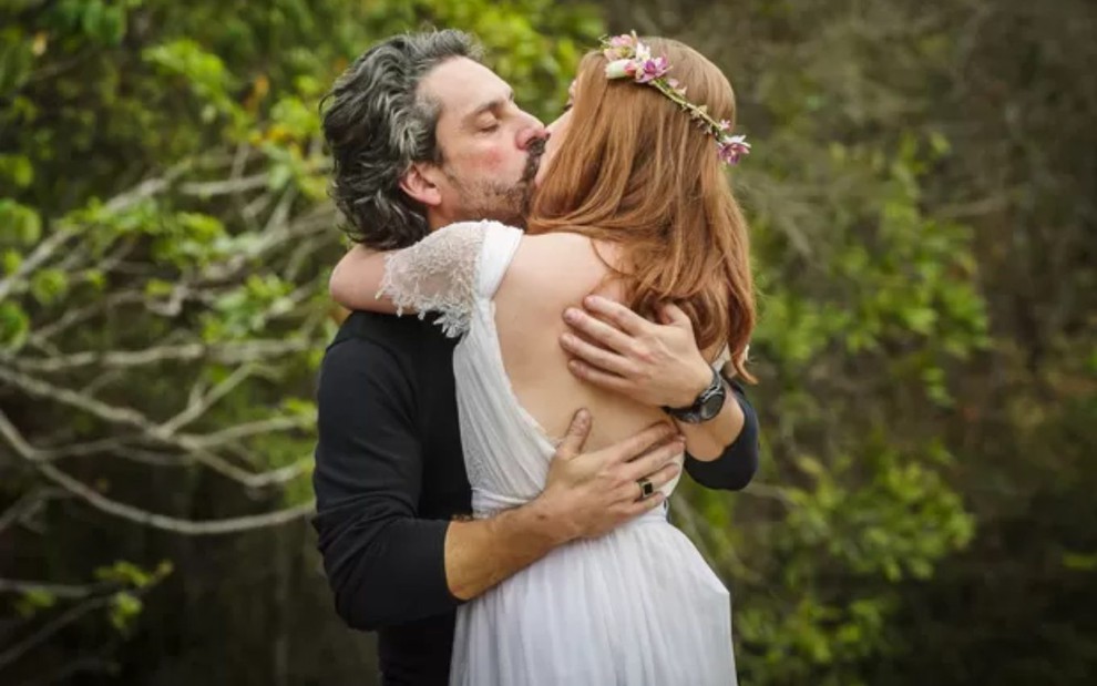 Os atores Alexandre Nero e Marina Ruy Barbosa em cena de beijo em área externa e arborizada em Império