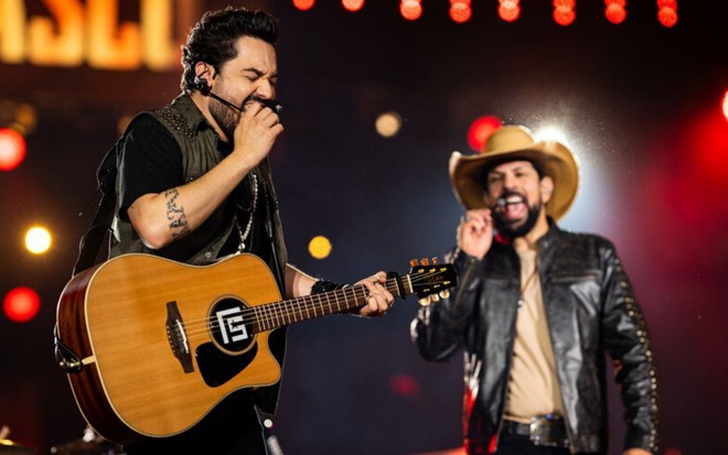 Em primeiro plano, Fernando toca violão e canta em show de novembro de 2019; ao fundo, Sorocaba canta