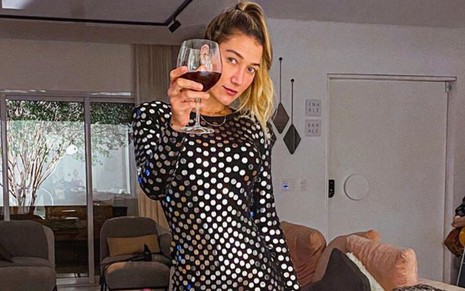 A influencer digital Gabriela Pugliesi de vestido de festa prata e preto segurando uma taça de vinho 