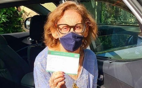 A atriz Laura Cardoso, de máscara, mostra certificado de que tomou a vacina contra o novo coronavírus neste sábado (6)