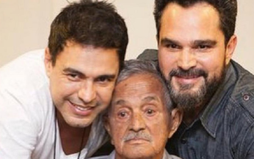 Foto dos cantores Zezé Di Camargo e Luciano Camargo abraçados com o pai, Francisco José Camargo (ao centro)