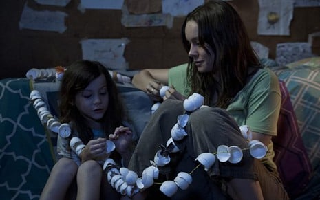 Jacob Tremblay como Jack e Brie Larson como Joy, sentados no chão e entrelaçados por um fio amarelo transpassado por cascas de ovos