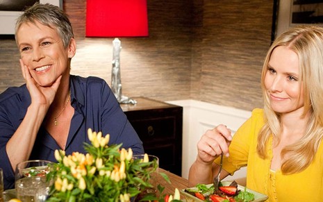 Sentadas em uma mesa de jantar, Jamie Lee Curtis e Kristen Bell sorriem em cena do filme Você De Novo