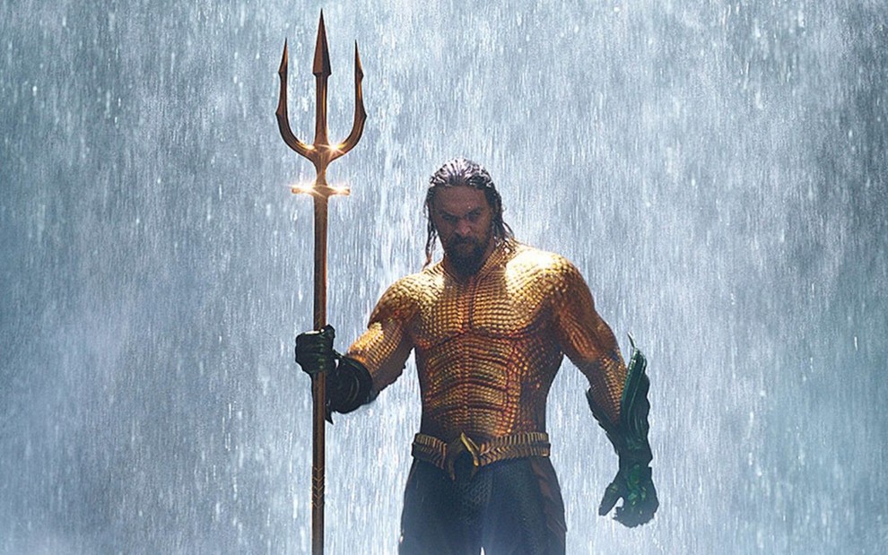 Jason Momoa segura um tridente e está em frente a uma queda de água em cena do filme Aquaman (2018)