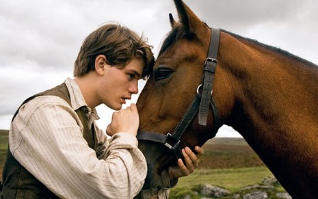 Albert (Jeremy Irvine) encosta a testa na cabeça de um cavalo em cena do filme Cavalo de Guerra (2012)
