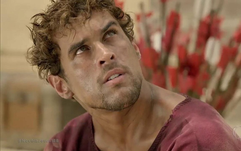 O ator Felipe Roque com rosto sujo e expressão séria em cena da novela Jesus, como Caius