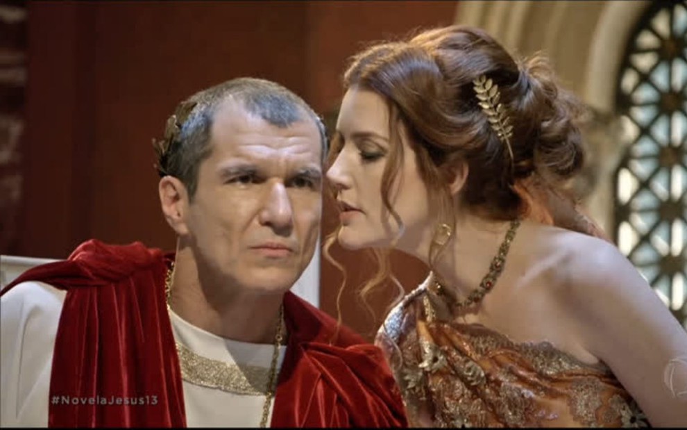 O ator Nicola Siri com expressão séria, a atriz Larissa Maciel ao lado dele, sussurando algo no ouvido, em cena de Jesus